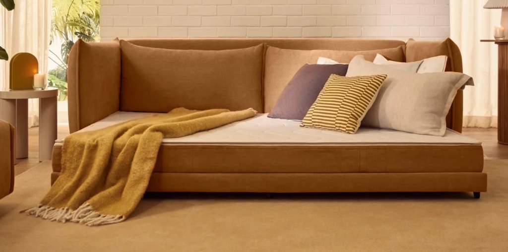 Modern bedroom with a low-profile upholstered bed, layered pillows, and a cozy throw blanket in a warm neutral interior.