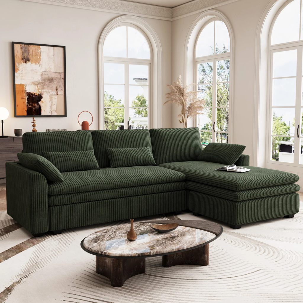 Dark green corduroy sectional sofa with chaise lounge in a bright living room featuring arched windows and a marble coffee table.