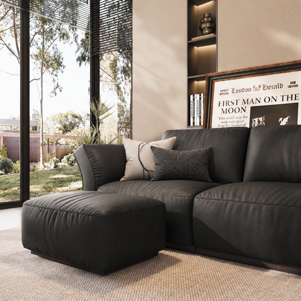 Dark gray leather sectional sofa with matching ottoman, neutral textured rug, black and cream pillows, and natural greenery in a modern earthy living room.