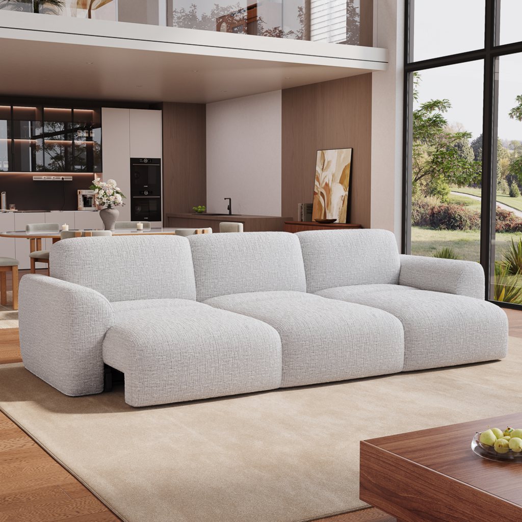 Light gray three-seater power sofa bed with one seat extended for lounging in a modern open-plan living room with floor-to-ceiling windows.