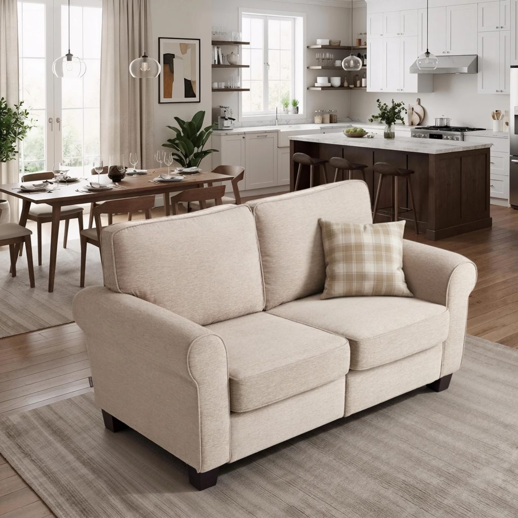 Beige two-seater loveseat with rolled arms and plush cushions in an open-plan living room with a dining area and modern white kitchen.