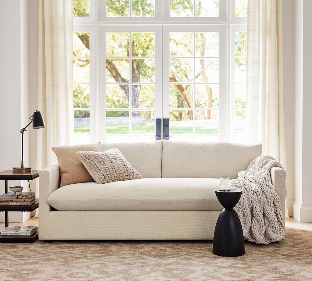Cream sofa with a wide bench cushion, textured pillows, and a knit throw in a bright living room with French doors.