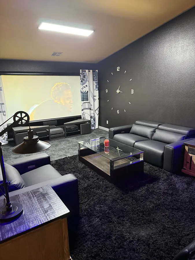 Black leather sofas and recliners arranged around a coffee table in a small home theater with a projector screen.
